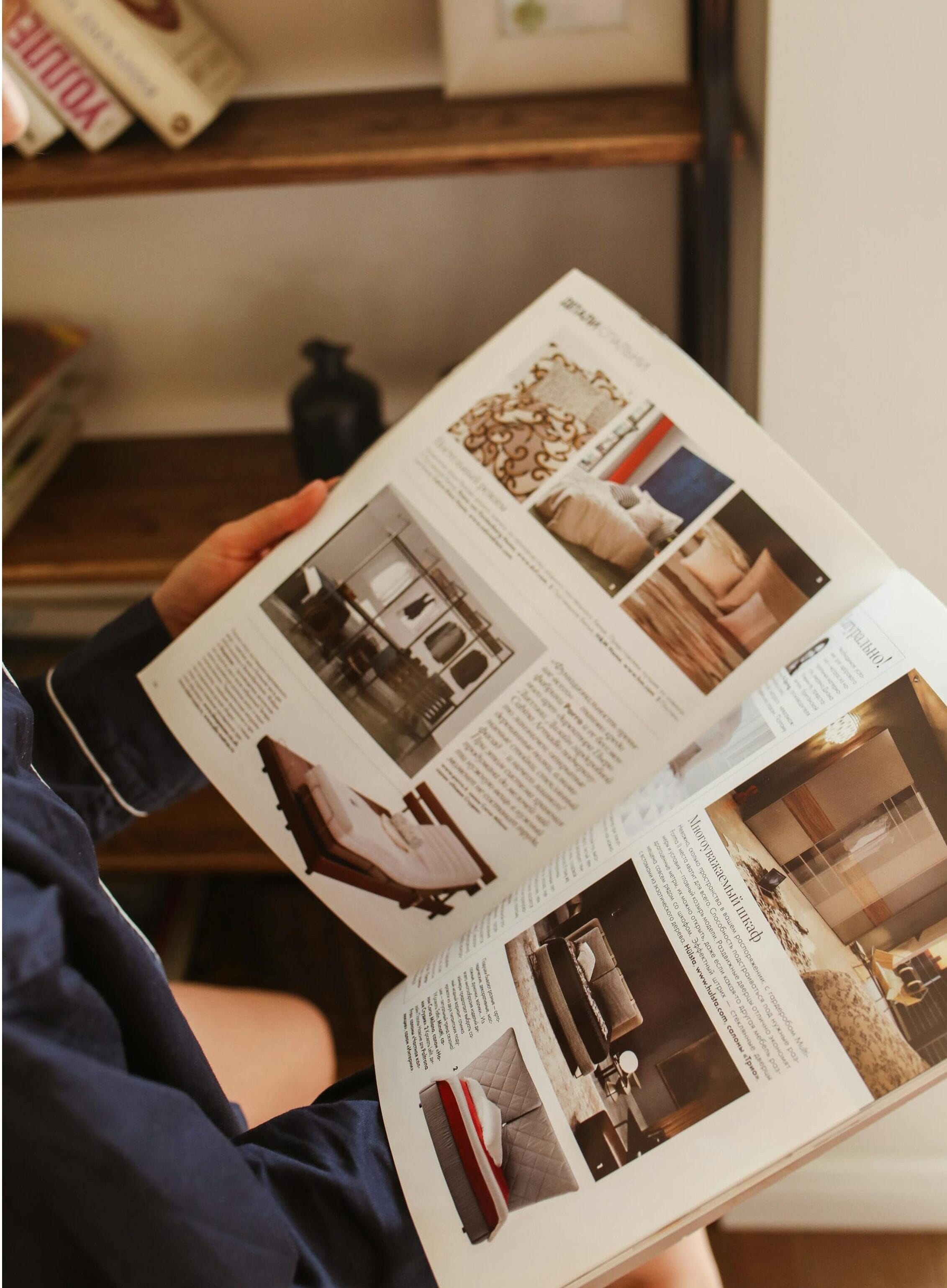 Person holding an open magazine without using their hands, with a bookcase in the background.